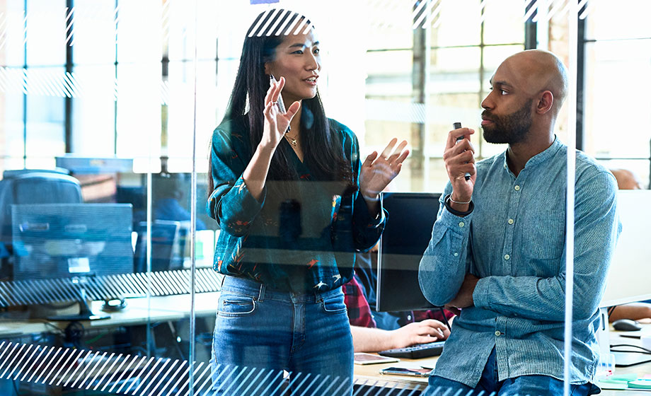 Asian and Black young professionals working on a clear whiteboard in an office