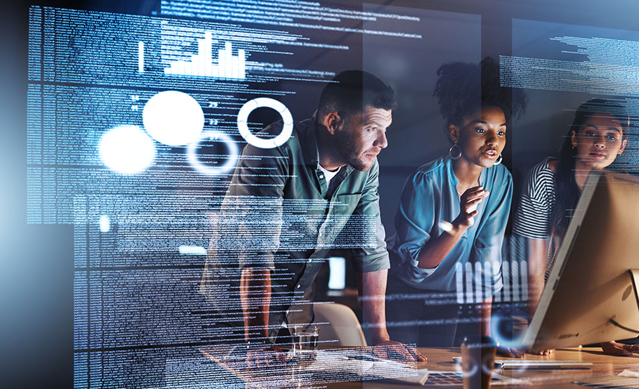 Three young working professionals working on a computer with hologram of data chart at left