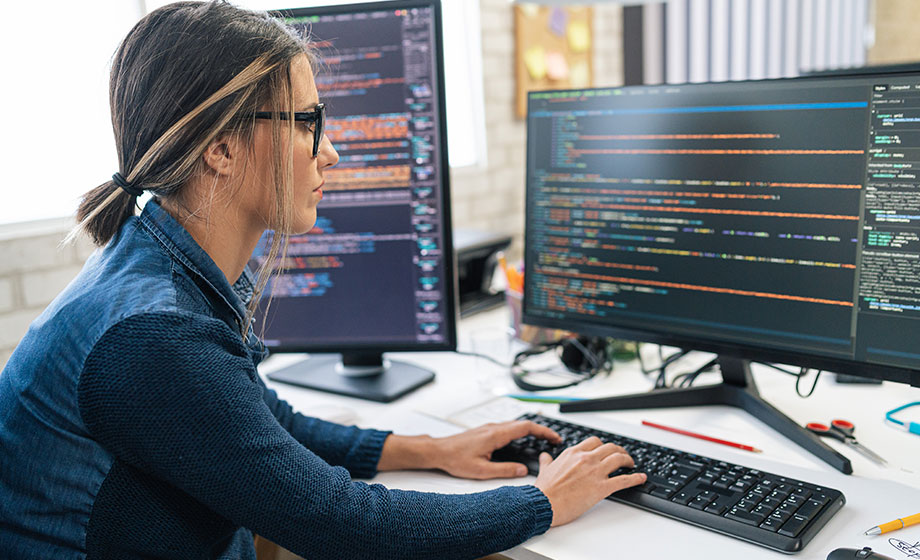 Young female professional working on code on multiple computer screens