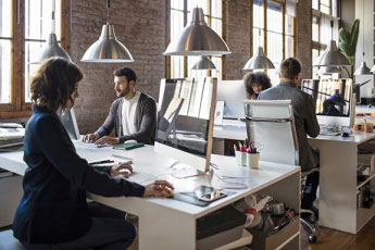 Workers at desks on computers in a brick-faced office building