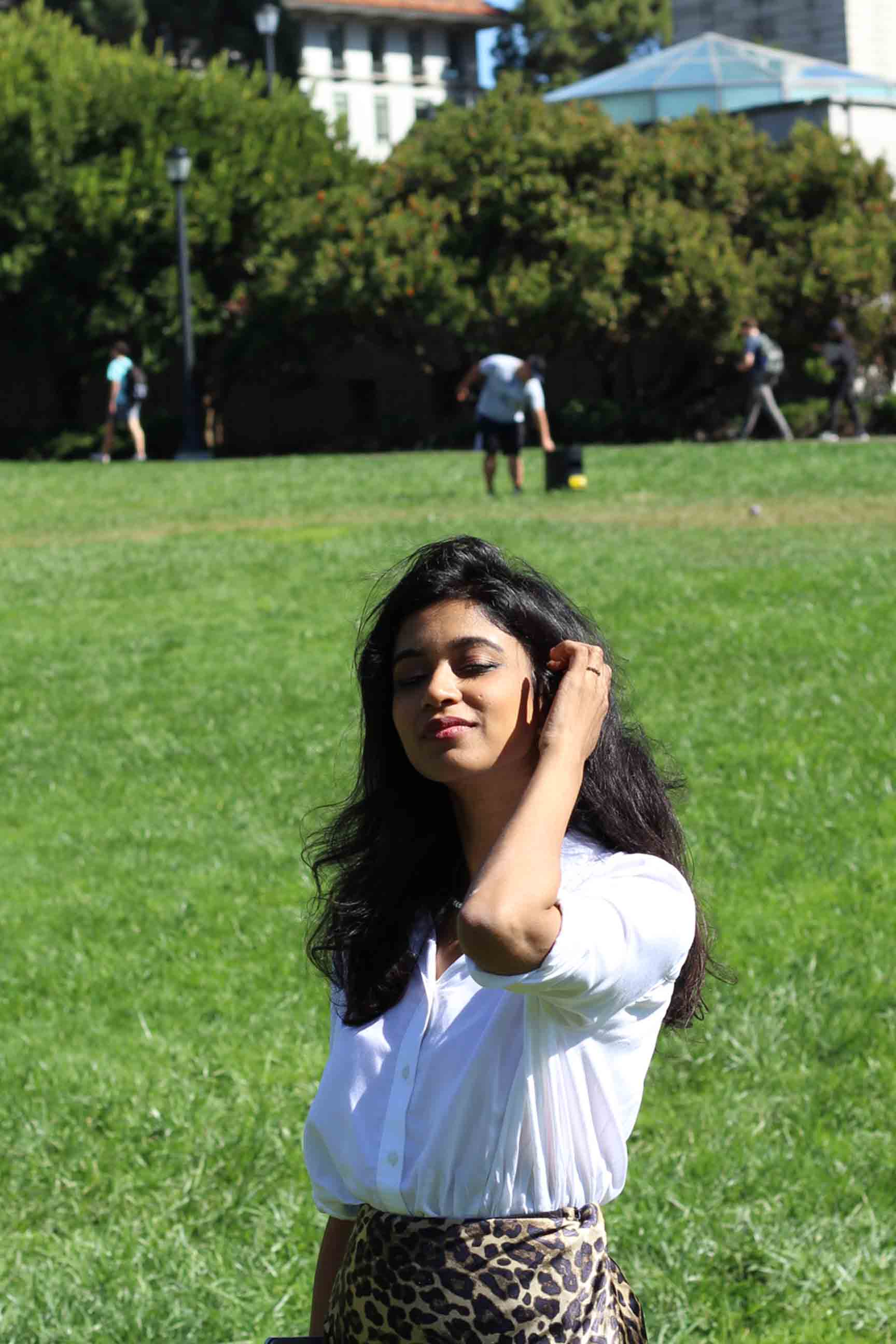 A girl standing in the Berkeley campus lawn with the Campanile in the background