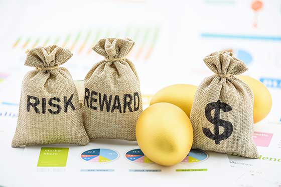 Photo of risk, reward and money bags on top of stock market printouts