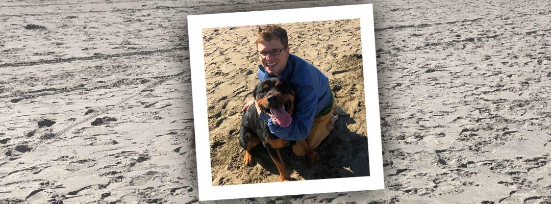Post-Bacc Health Professions student, scholarship winner Matt Klinkel on a beach with a dog