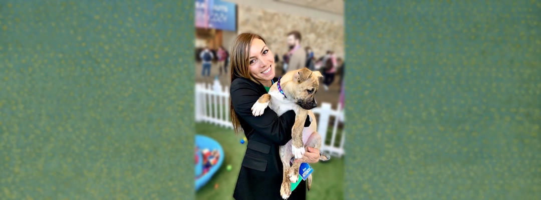 Marketing graduate Camille Rasmussen holding a puppy in front of a green background