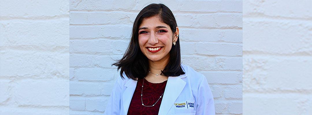 Post-Baccalaureate Health Professions Program alumna Ferheen Abbasi wearing a UC Davis Health blazer, in front of white brick wall