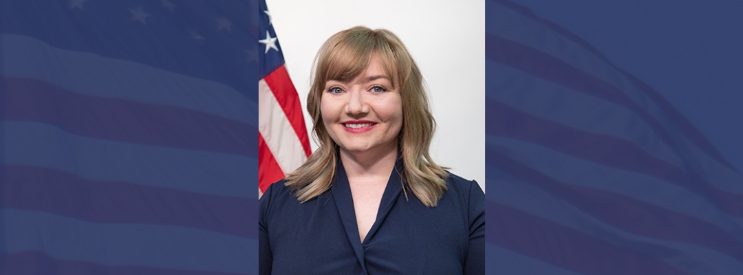 Headshot of Lacy Kelly Ramos in front of U.S. flag on blue background