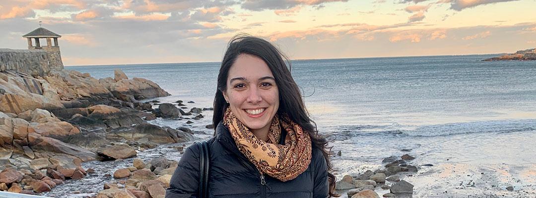Photo of Post-Bacc Counseling and Psychology program graduate Lisell Perez-Rogers standing on an oceanfront with sunset and rocks in background