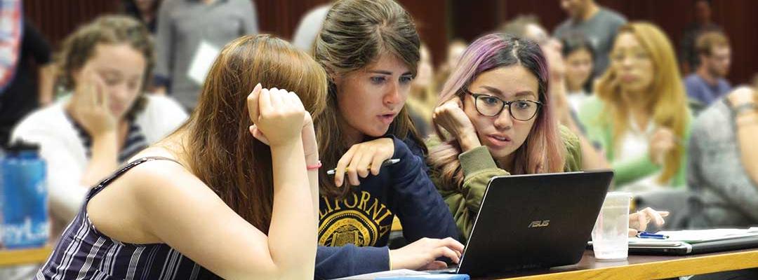 Three female students in a Berkeley classroom looking at a laptop
