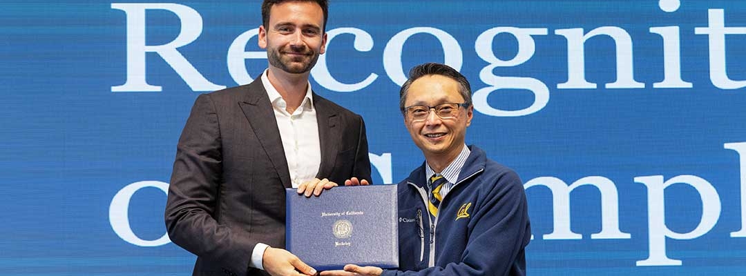 Lucas Mortier on left with Henry Tsang standing in front of blue background accepting a diploma