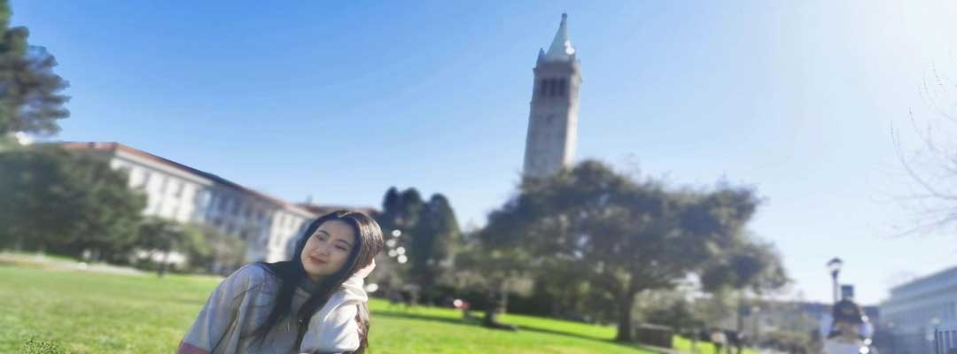 Xiaole Guo sitting on lawn in front of UC Berkeley Campanile