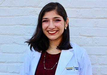 Post-Baccalaureate Health Professions Program alumna Ferheen Abbasi wearing a UC Davis Health blazer, in front of white brick wall