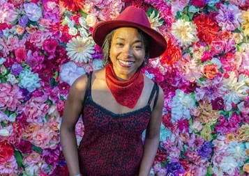 Photo of Sandra Titre standing in front of a wall made of flowers