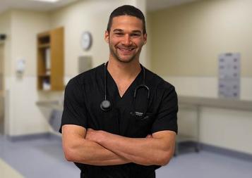 Alexander Lipson in his nursing outfit standing in front of a clinical setting