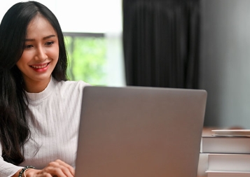 Stock image of a female Asian writer writing on laptop with books on table
