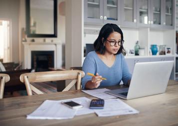 Woman sitting at kitchen table looking at laptop working on financial reports