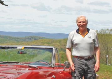 Writing certificate graduate and author Bill Truran next to a red sports car with hills behind him. Photo.