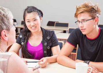 Photo of education counselor sitting at a table with a young woman and a young man