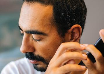 Photo of man eyes closed, turned away from cell phone, listening with left ear