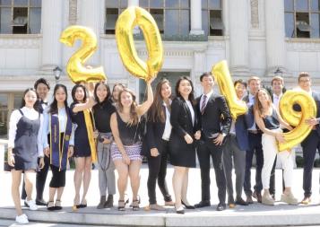 Karin and the rest of the BHGAP students smiling and posing for a picture in front of Doe Memorial Library, holding 2019 balloons in their hands.
