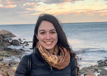 Photo of Post-Bacc Counseling and Psychology program graduate Lisell Perez-Rogers standing on an oceanfront with sunset and rocks in background