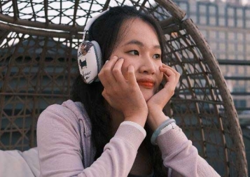 Photo of Lydia Bao wearing headphones while sitting in a rattan chair