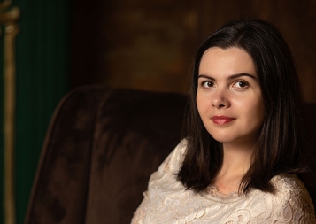 Photo of Polina Stepanova wearing a white dress while sitting in a brown suede chair