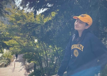 Victoria Kim sitting on railing on Berkeley campus with trees surrounding her