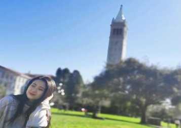 Xiaole Guo sitting on lawn in front of UC Berkeley Campanile