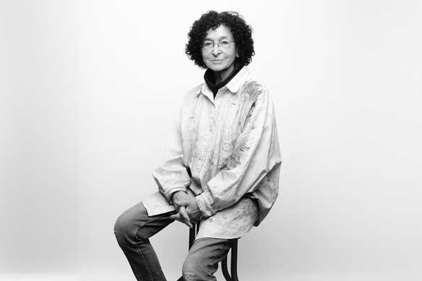 Photo of Elisabeth Koss sitting on a stool in front of a gray background