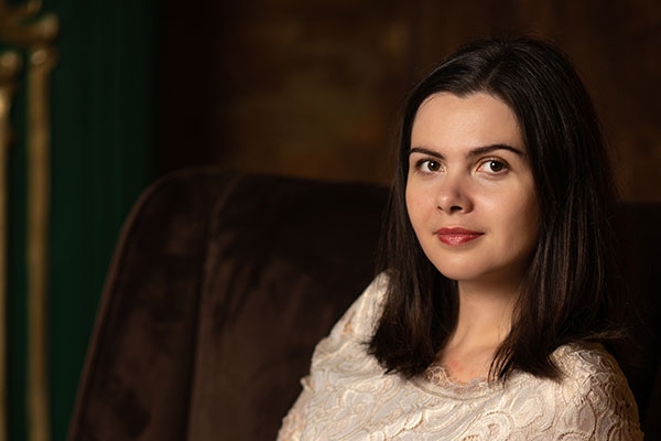 Photo of Polina Stepanova wearing a white dress while sitting in a brown suede chair