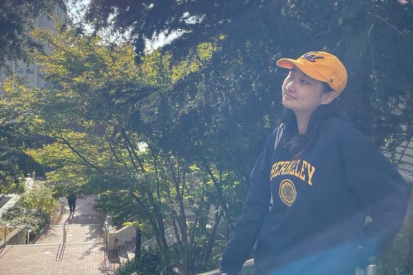 Victoria Kim sitting on railing on Berkeley campus with trees surrounding her