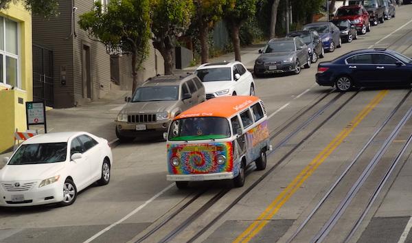 A rainbow painted van drives down a hilly San Francisco street