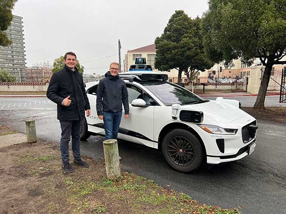 Sebastian Sartor and friend posing in front of a self-driving autonomous car