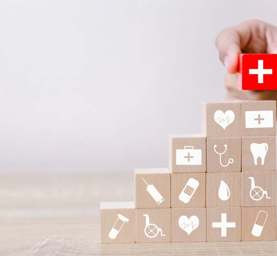 Hand stacking red block with white cross on stack of wooden blocks with medical logos