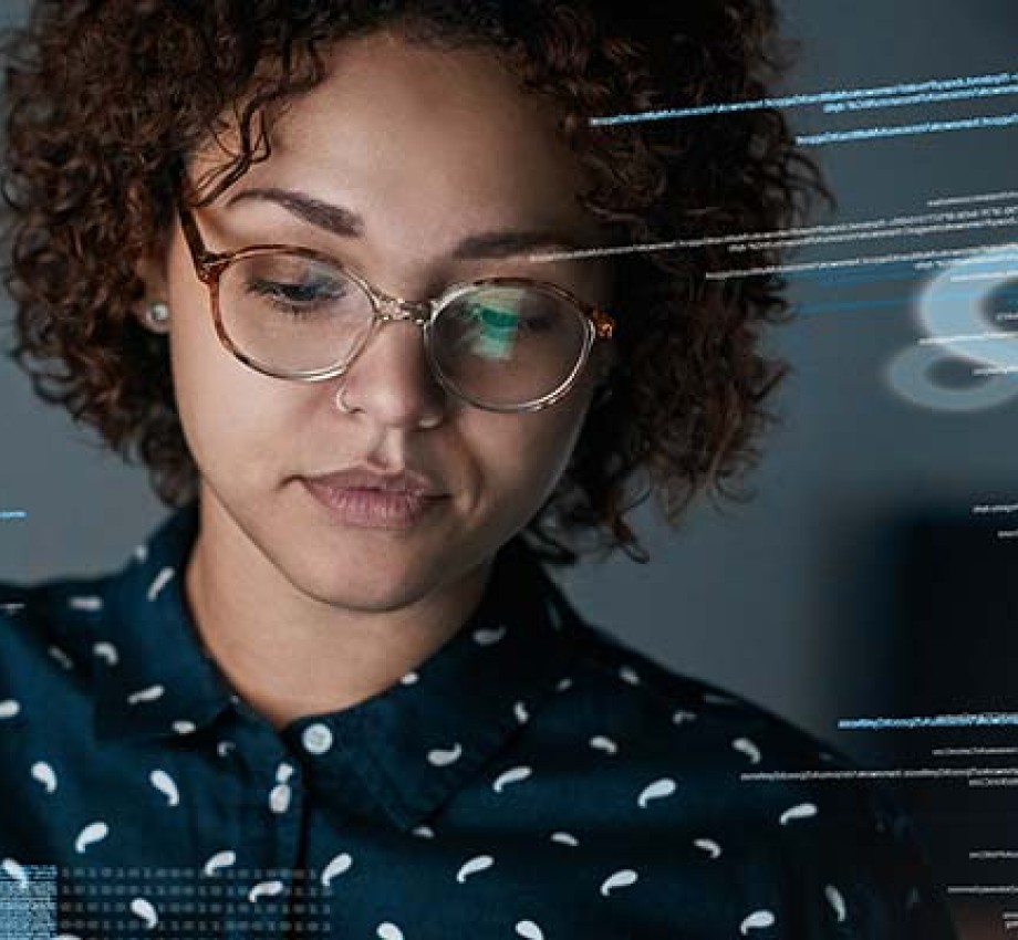 A woman with curly hair and glasses with a computer screen reflection surrounding her