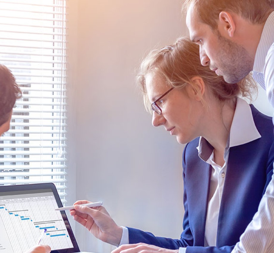 Three staff members gather around a laptop computer looking at a project chart