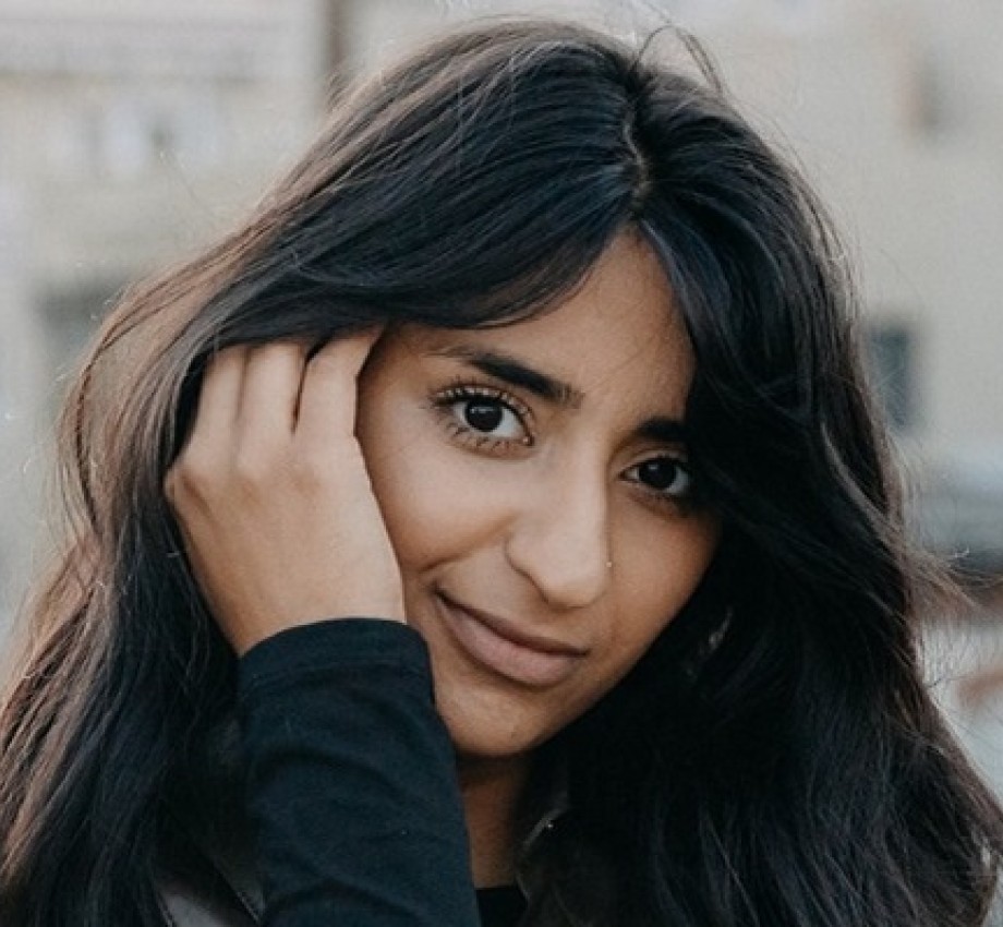 UX Design graduate Sana Maqsood outside with hand behind ear, in long dark hair. Photo.