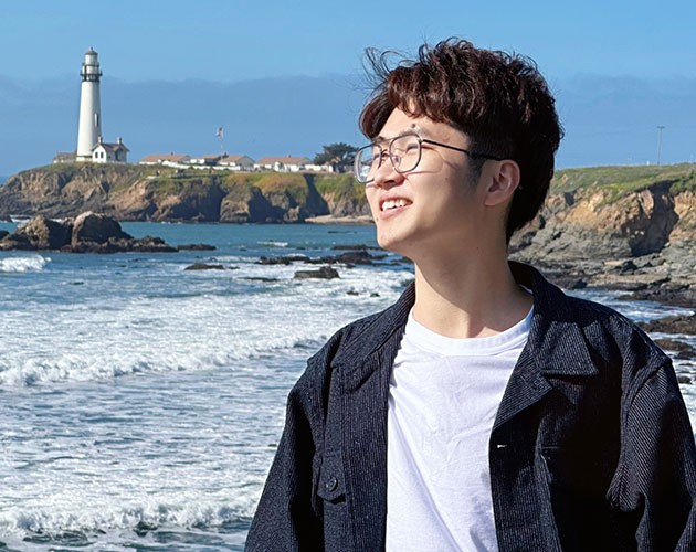 Chuang Lyu stands in front of a light tower at the Pacific Ocean shore