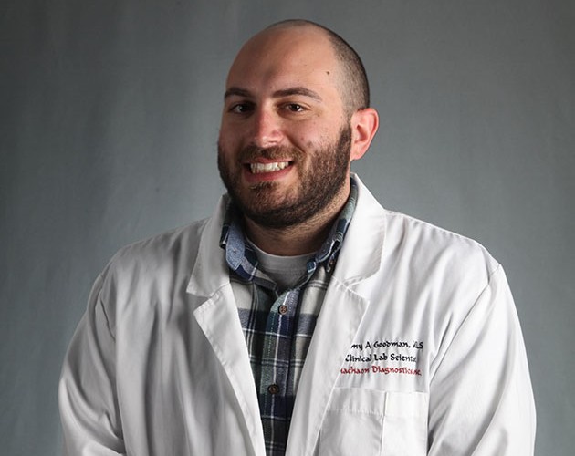 Photo of Jeremy Goodman wearing white lab coat in front of gray background