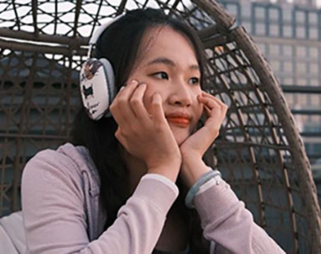 Lydia Bao wearing headphones while sitting in a round wicker chair