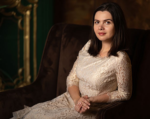 Photo of Polina Stepanova wearing a white dress while sitting in a brown suede chair