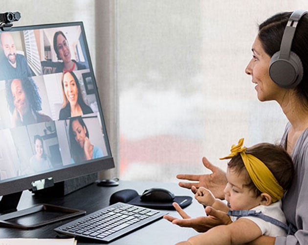 Photo of a woman with infant on her lap, wearing headphones while on video conference on computer screen