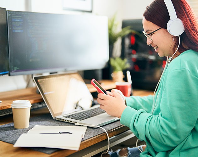 Milleniall woman working on a laptop while checking phone