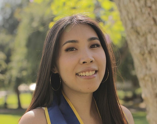 Khatu Nguyen wearing a graduation sash while posing in front of a tree