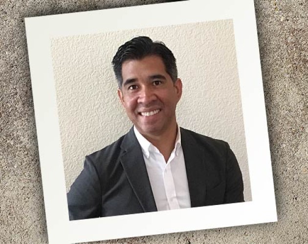 Square photograph on a granite surface at a tilt featuring College Admissions instructor Armando Diaz in an open-collar shirt and suit jacket