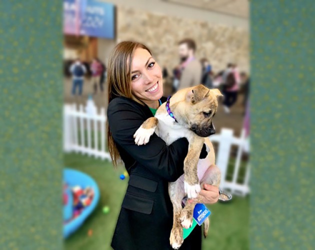 Marketing graduate Camille Rasmussen holding a puppy in front of a green background