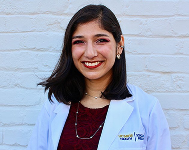 Post-Baccalaureate Health Professions Program alumna Ferheen Abbasi wearing a UC Davis Health blazer, in front of white brick wall