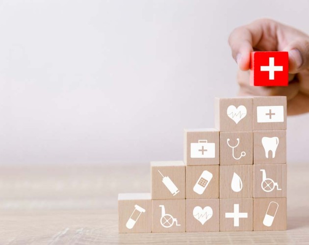 Hand stacking red block with white cross on stack of wooden blocks with medical logos