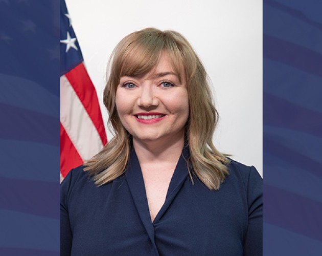 Headshot of Lacy Kelly Ramos in front of U.S. flag on blue background