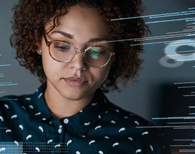 A woman with curly hair and glasses with a computer screen reflection surrounding her